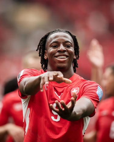 Smiling Switzerland national football player in a red jersey celebrating a goal on the pitch.