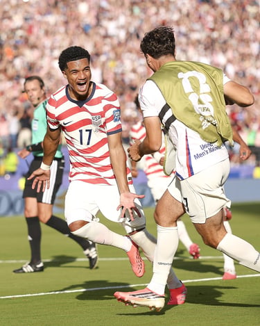 USMNT soccer player Malik Tillman celebrating a goal in a USA jersey during an international match.