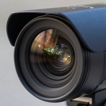 Close-up macro shot of a high-quality CCTV camera lens, showing intricate glass reflections and a professional slate blue casing.