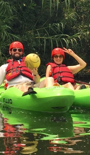 Two kayakers smiling in green kayaks while holding up a ball recovered from the river.