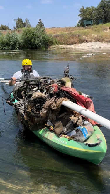 Kayaker hauling debris and trash from a river during a waterway cleanup effort.