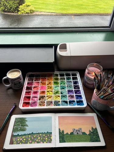 An image of coffee, a lit candle and some colourful paints