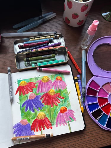 Coneflowers painted in a sketchbook, surrounded by art supplies