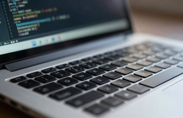 A close-up of a silver laptop keyboard with soft focus on a digital screen displaying code, illuminated by a soft slate blue glow.