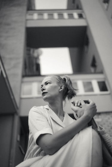 Black and white portrait of a woman looking away against a backdrop of urban architecture.
