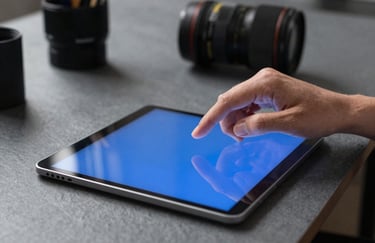 A close-up photograph of a professional's hands using a high-tech tablet in a North American / US co-working space. Slate grey surfaces and vibrant blue screen light.