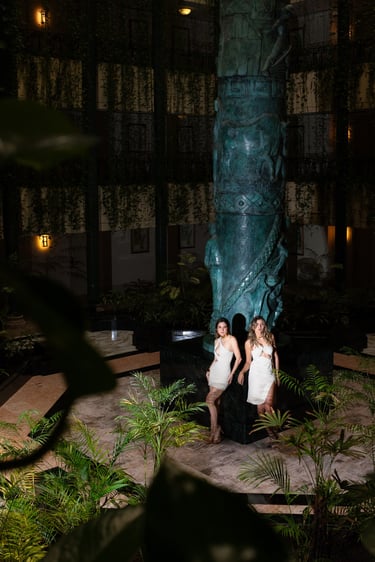 Dos modelos posando de noche con vestidos de gala en el jardín iluminado de un hotel de lujo Kempinski en Cancún.