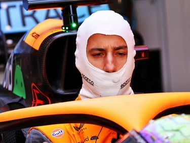 Formula 1 driver wearing a white Sparco fireproof balaclava inside a McLaren racing car cockpit.