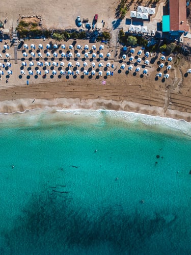 Aerial view of a tropical beach resort with rows of white umbrellas and turquoise ocean water.