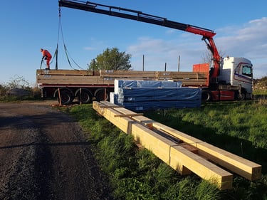 En kranlastbil aflæsser stakke af byggetræ og tømmer på en byggeplads.