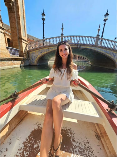 A woman in a white dress rowing a small boat on the canal at Plaza de Espana in Seville, Spain.