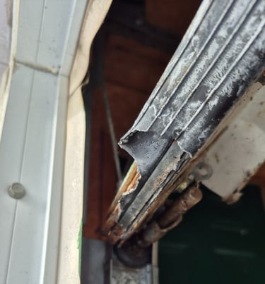 Damaged garage door bottom seal and rusty metal retainer requiring repair or replacement.