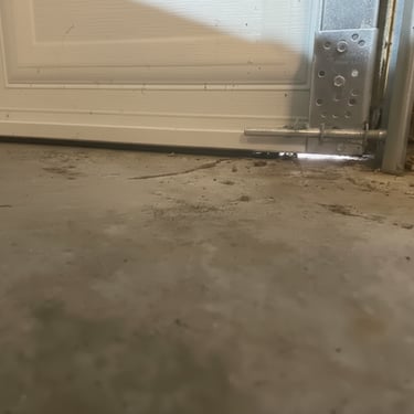 A white garage door with a gap at the bottom showing a worn weather seal on a concrete floor.