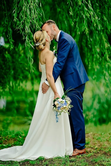 Brautpaar küsst sich unter Bäumen am Seeufer in Möhnesee.