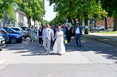 Hochzeitsfotograf Möhnesee: Brautpaar geht Hand in Hand voran; jubelnde Hochzeitsgesellschaft folgt ihnen auf der Straße.