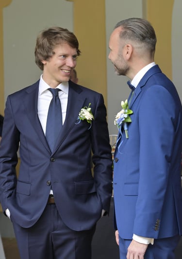 Zwei Hochzeitsgäste im Anzug stehen beim Sektempfang im Gespräch und lächeln sich an.