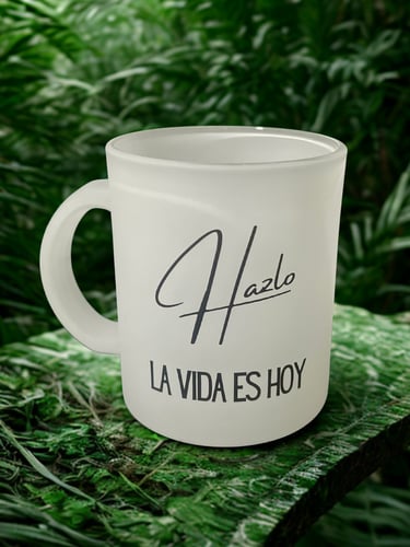 Frosted glass coffee mug with Spanish quote Hazlo La Vida Es Hoy set against a lush green forest background.