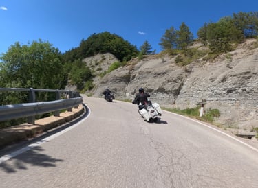 Zwei Harley Fahrer auf ihrer Tour in einer Kurve in bergiger Landschaft.