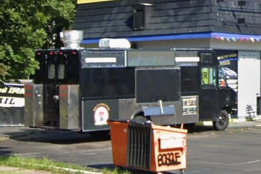 A black gourmet food truck parked in a city lot, featuring a professional kitchen setup and side serving window.
