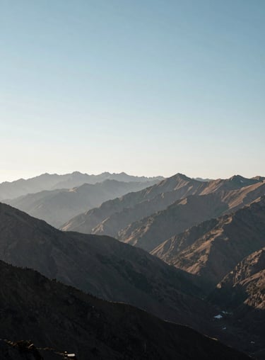 A scenic view of a mountain range in the Andes under a clear, soft light blue-white sky, conveying a sense of perspective and peace.