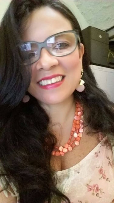 Mulher sorridente usando óculos e um colar de contas rosa em camadas, com longos cabelos escuros.