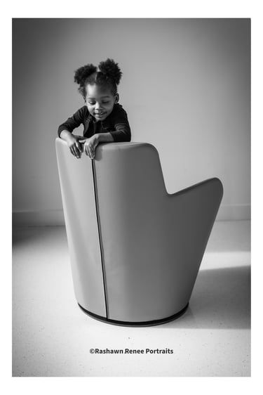 Black and white portrait of a young girl leaning on a modern chair in a studio.