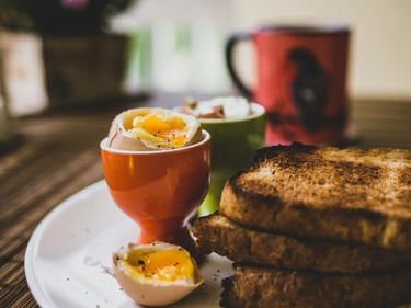 Soft boiled egg in an orange egg cup with whole wheat toast soldiers on a breakfast plate.