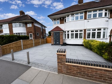Modern grey stone block paved driveway in front of a white semi-detached house with a new brick wall.