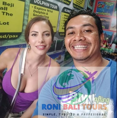 Smiling woman and tour guide posing for a selfie in front of a Bali travel excursion billboard.