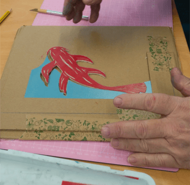 Person assembling pieces of cut lino together in a jigsaw print shaped like a fish