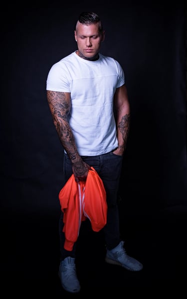 Porträt eines muskulösen Mannes mit Tattoos, weißem T-Shirt und Jeans, im Fotostudio Berlin aufgenommen.