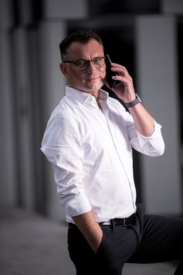 Businessfoto eines Mannes im weißen Hemd mit Brille, telefonierend vor moderner Architektur in Berlin.