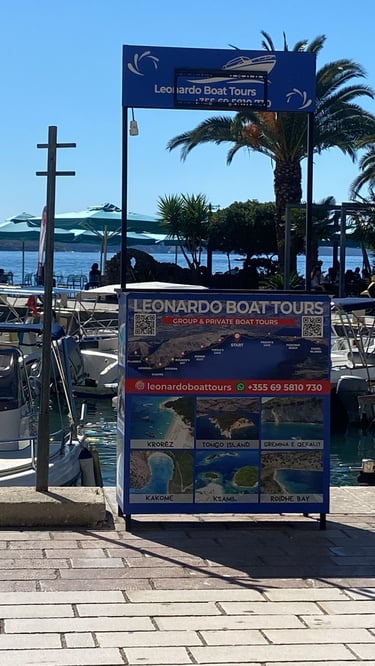 Leonardo Boat Tours sign at a marina showing a map and photos of Ksamil and Krorez boat trip destinations.