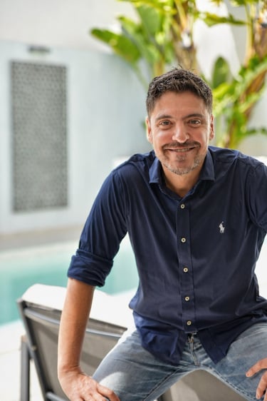Smiling man in a navy blue Ralph Lauren polo shirt sitting outdoors by a swimming pool.