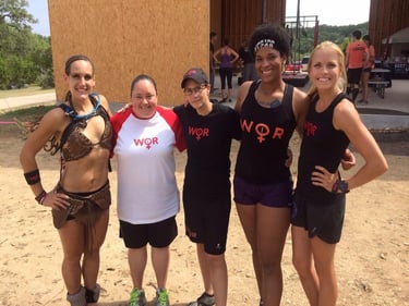 Five diverse female athletes smiling together at an outdoor OCR mud run event wearing WOR team shirts.