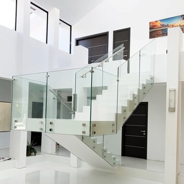 Modern white floating staircase with frameless glass railings and stainless steel hardware in a luxury home.