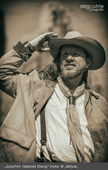 Charakter-Portrait Joachim Klang derjoe im Western-Outfit mit Cowboyhut, aufgenommen outdoor im Vintage-Stil.