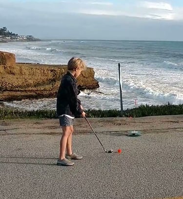 Kid putting street golf ball on a pavement near ocean
