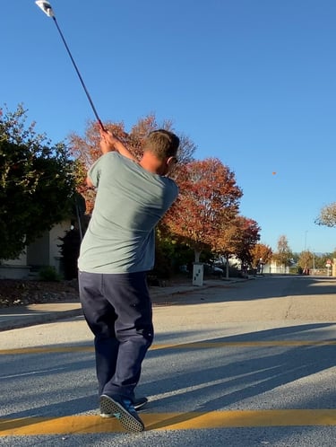 Man downswing a street golf ball on a street with Golf Club Iron