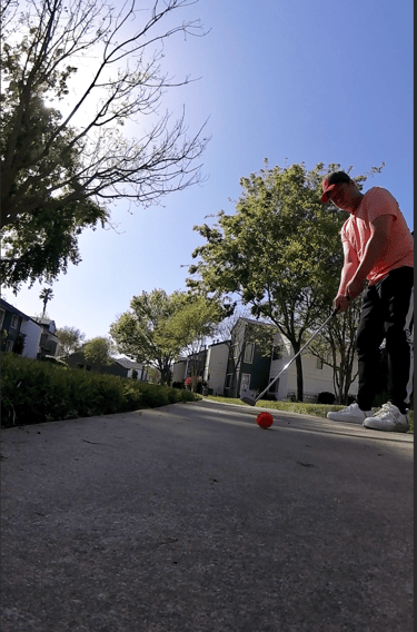 Young man putting a street golf ball on a sidewalk in an apartment complex
