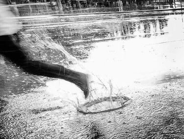 Monochrome image of a lone figure splashing though a puddle in the street.