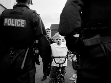 Street photography in black and white, capturing a a young boy on a bike confronting police.