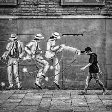 Black and white photo of wall mural showing person seemingly kicking a passer-by.
