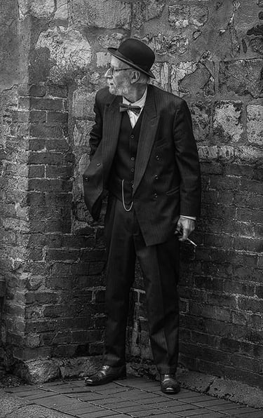 Candid black and white street photo of a dapper gentleman; a sneaky cigarette?
