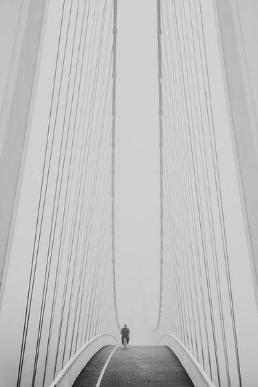 Dramatic monochrome image of a lone cyclist riding over a suspension bridge.