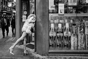 Monochrome photo of leggy girl peering into a shop door from a city street.