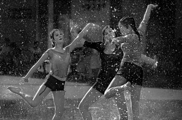 Black and white candid street scene capturing young girls dancing in the rain.