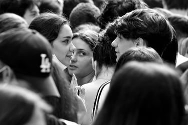 Black and white street image of girl in a crowd watching another young couple.