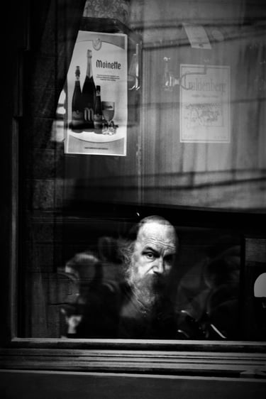 Monochrome shot of a bearded man through a shop window.