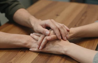 A close-up photography of two people's hands resting on a wooden table in a supportive gesture, conveying connection and trust.